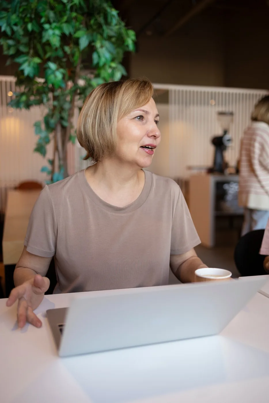 A woman talking across her laptop in a bright café