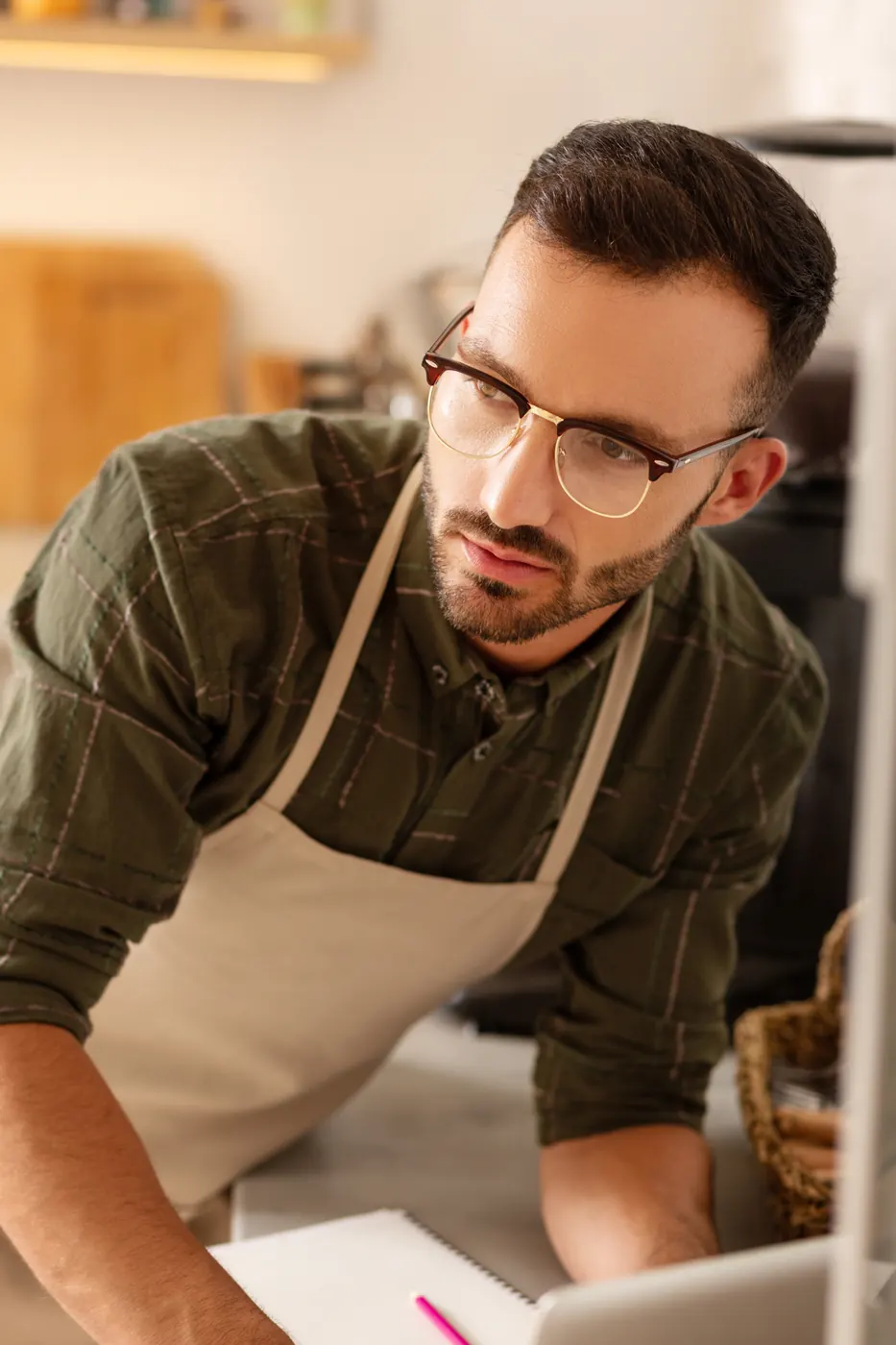 A man in glasses and an apron reviewing notes at his counter