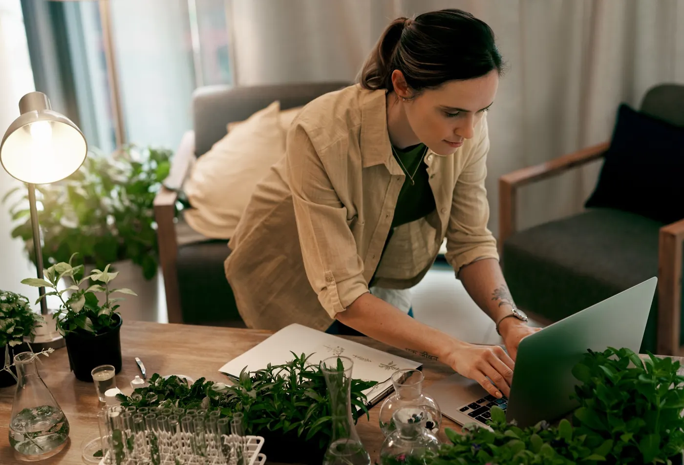 A woman working on a laptop at a table full of potted herbs